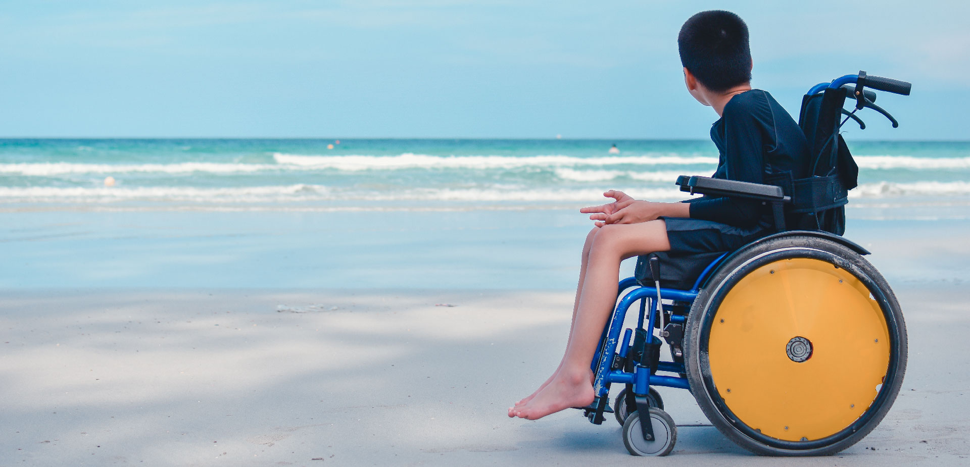 Boy in a wheelchair on the beach looking out at the sea