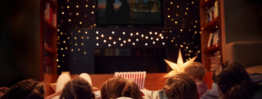 Four kids lieing on pillows while watching a movie which is being projected on the wall